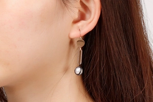 Detail of elegant long pearl earrings with oval metal links on model's ear