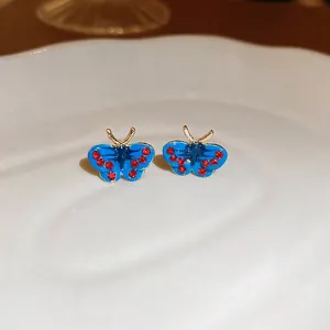Elegant gold butterfly stud earrings with bright blue wings and red crystal accents