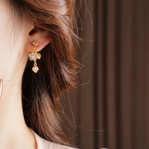 Close-up of elegant gold flower tassel earrings with gems worn by a model in soft lighting