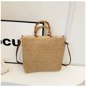 Detail of woven straw tote bag featuring bamboo handles and brown faux leather strap