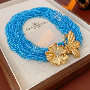 Detail of multi-layer sky blue beaded necklace with golden butterfly and floral charms