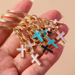 Close-up of hand holding colorful enamel cross keychains with gold-toned alloy finish