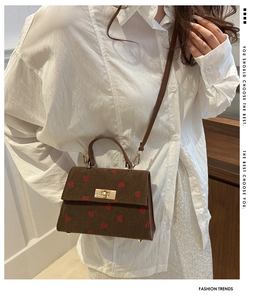Close-up of brown corduroy handbag featuring red strawberry patterns and a gold lock