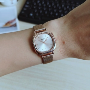 Close-up of a women's rose gold square quartz watch with a mesh strap on a wrist