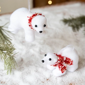 White flocked polar bear Christmas ornaments with red scarves hanging on a festive tree