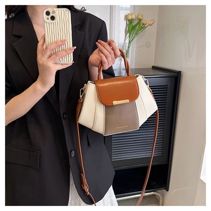 Detail showing contrast color handbag with brown flap and grey body held by a model