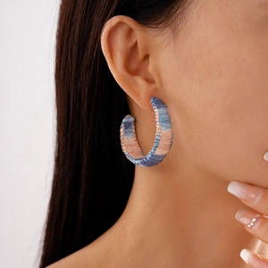 Close-up of bohemian C-shaped woven earrings in blue and pink on model's ear