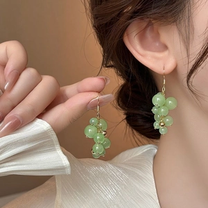 Macro detail of grape-shaped earrings featuring green beads and golden hooks on model
