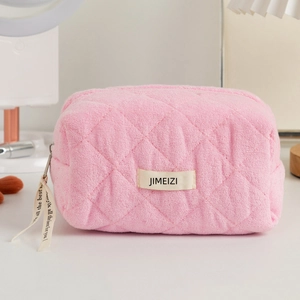 Detail of pink quilted plush makeup bag with branded tag and decorative zipper ribbon