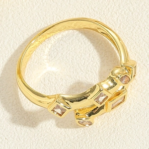 Detail of gold geometric ring with square and round zircon stone inlay on textured surface