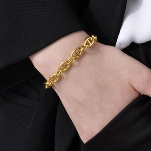 Close-up of 18k gold-plated pig nose link bracelet on wrist with elegant black blazer
