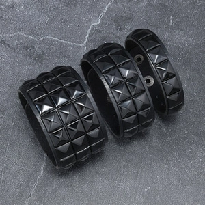 Detailed view of three black leather punk bracelets with metallic pyramid studs on stone background