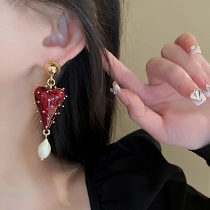 Détail d'une boucle d'oreille cœur rouge avec clous dorés et perle baroque blanche