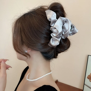 Macro shot of silver-grey satin cloud scrunchie showing fine fabric texture on a bun