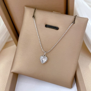 Detail of silver heart pendant with clear gemstone on gold display pad in gift box