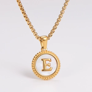 Macro shot of gold stainless steel necklace featuring a round white shell pendant with letter E