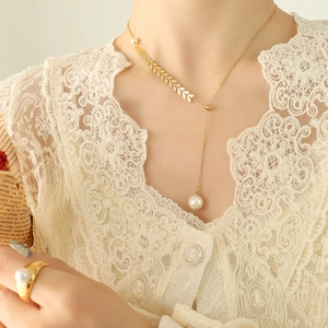 Elegant gold necklace and ring set with wheat leaf charms and white pearls on a model