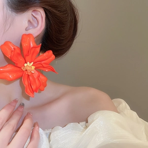 Close-up of oversized orange acrylic flower earring worn by a model for a resort style look