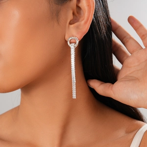 Close-up of dangling silver earrings with rectangular zircons on a female model