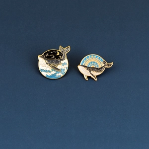 Detailed close-up of whale enamel pins with celestial starry sky and wave motifs