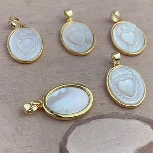 Oval white mother of pearl Sacred Heart pendants with gold plated borders on wood