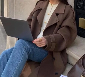 Manteau en laine marron pour femme porté avec un jean et un ordinateur en extérieur
