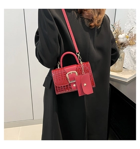 Détail du sac rouge à motif crocodile avec garniture dorée porté sur un manteau noir
