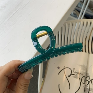 Détail d'une pince à cheveux en acrylique cyan foncé avec ressort doré en main