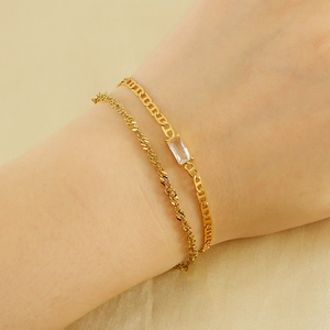 Double-layered gold chain bracelet set with rectangular zircon stone on flat fabric background