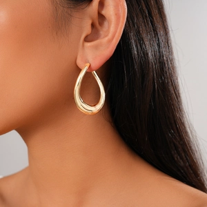 Close-up of a model wearing a polished gold teardrop earring with minimalist metal design