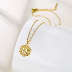 Detailed close-up of textured gold hexagonal pendant with letter M on ceramic cup