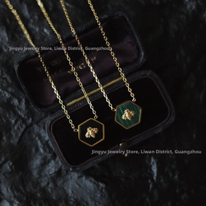 Close-up of hexagonal bee pendants with green and black enamel on gold necklaces