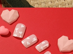 Detailed view of pink press-on nails with white heart patterns on a red background
