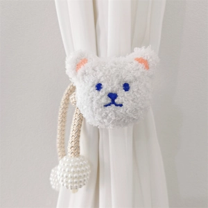 Close-up of plush white bear curtain tieback with blue embroidery and pearl ball tassels