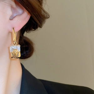Close-up of gold lion head earrings with square crystal on model in soft lighting