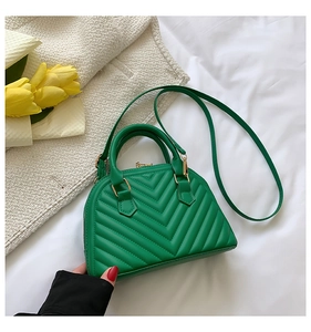 Detail of green quilted crossbody bag with V-shaped stitching and gold hardware