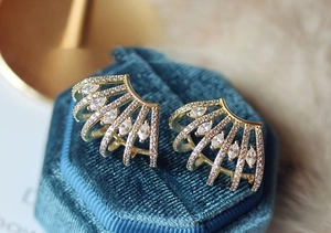 Detailed view of gold plated fan-shaped earrings with marquise zircon on blue velvet box