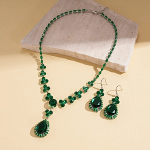 Detailed shot of green teardrop gemstone necklace and earrings on a textured stone surface