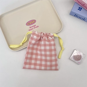 Detailed shot of pink gingham drawstring pouch with vibrant yellow cord on a beige tray