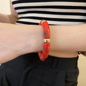 Close-up of a red acrylic geometric bracelet with gold metal accents on a model's wrist