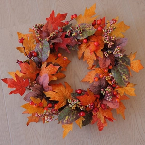 Detailed overhead shot of an autumn maple leaf wreath with red berries on light wood floor