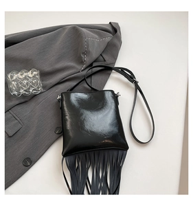 Detail of a black leather crossbody bag with long fringes and polished metal accents