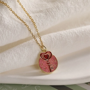 Detail of pink glitter heart and key enamel pendant on a golden chain necklace