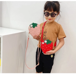 Close-up of a stylish strawberry-shaped crossbody bag worn by a young girl in red and pink
