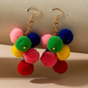Detail shot of colorful plush pom-pom earrings hanging on a display stand with gold hooks