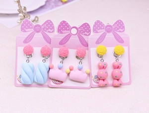 Detailed view of cute cream-colored cartoon rainbow unicorn and candy clip-on earrings
