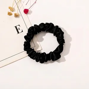 Detail of high-elastic black satin scrunchie with soft silk texture on white background