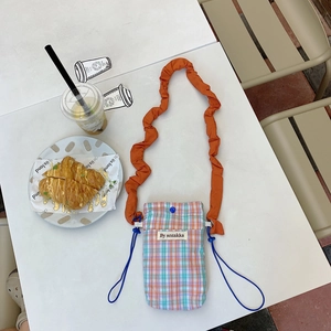 Detail of checkered crossbody phone bag with orange pleated strap on an outdoor table