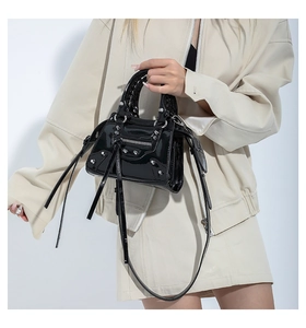 Detail of glossy black patent leather bag with metallic rivets and tassel zippers