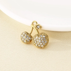 Close-up of a gold cherry charm pendant with clear rhinestones on a ceramic dish